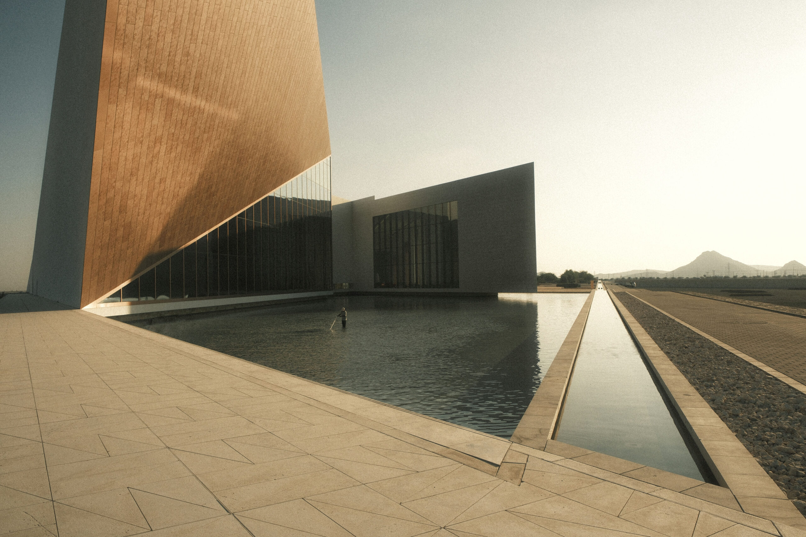 fotografia di architettura minimalista monumentale con volume inclinato e grande vasca d’acqua riflettente nel deserto al tramonto laura farina fotografa