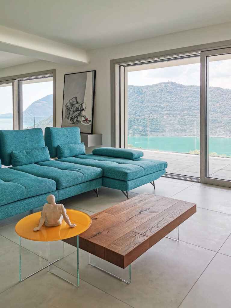 fotografia interno soggiorno moderno open space con divano blu tavolino legno illuminazione LED integrata nelle pareti vista lago laura farina architetto