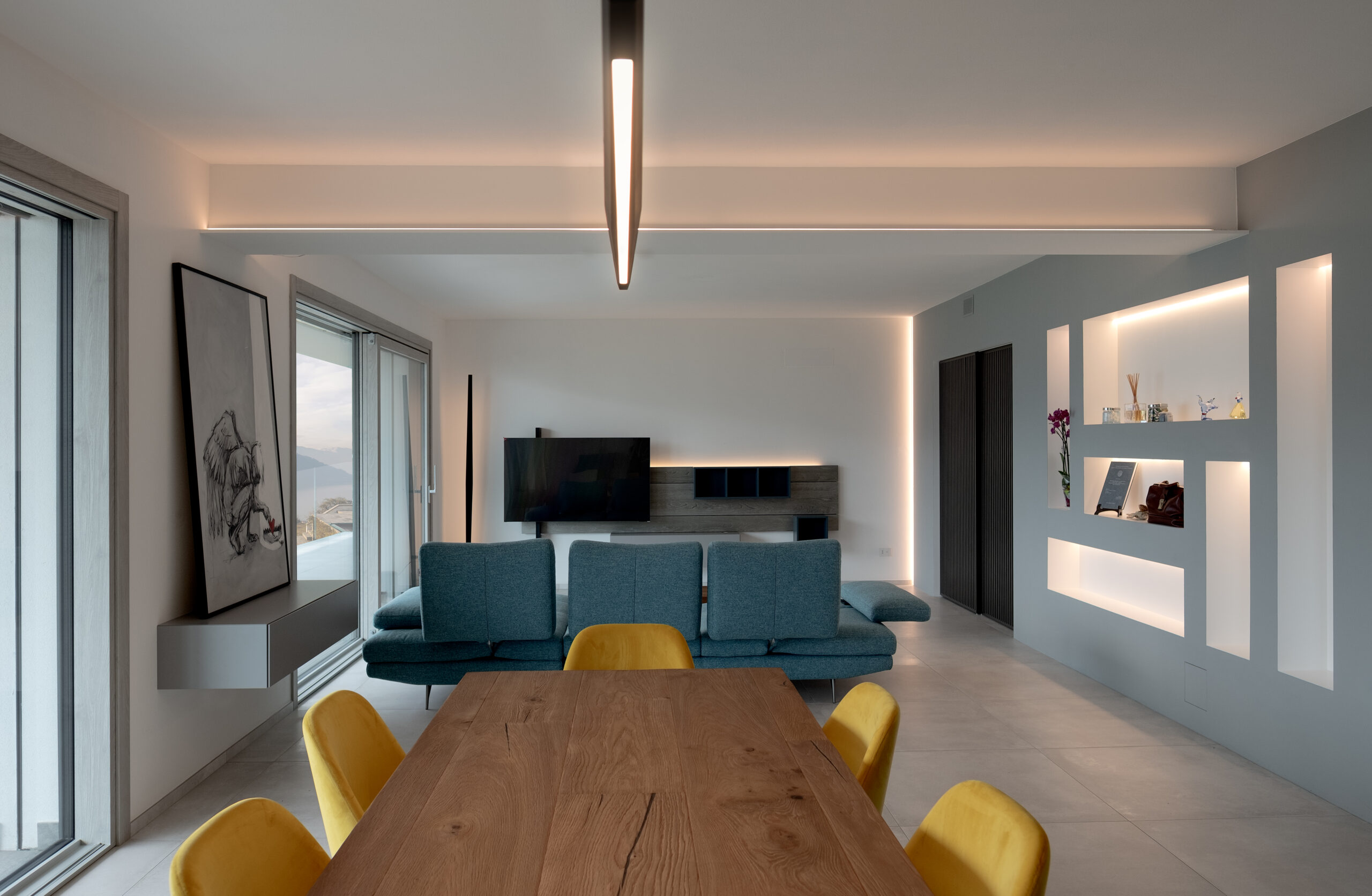 fotografia interno soggiorno moderno open space con divano blu tavolo legno sedie gialle illuminazione LED integrata nelle pareti laura farina architetto